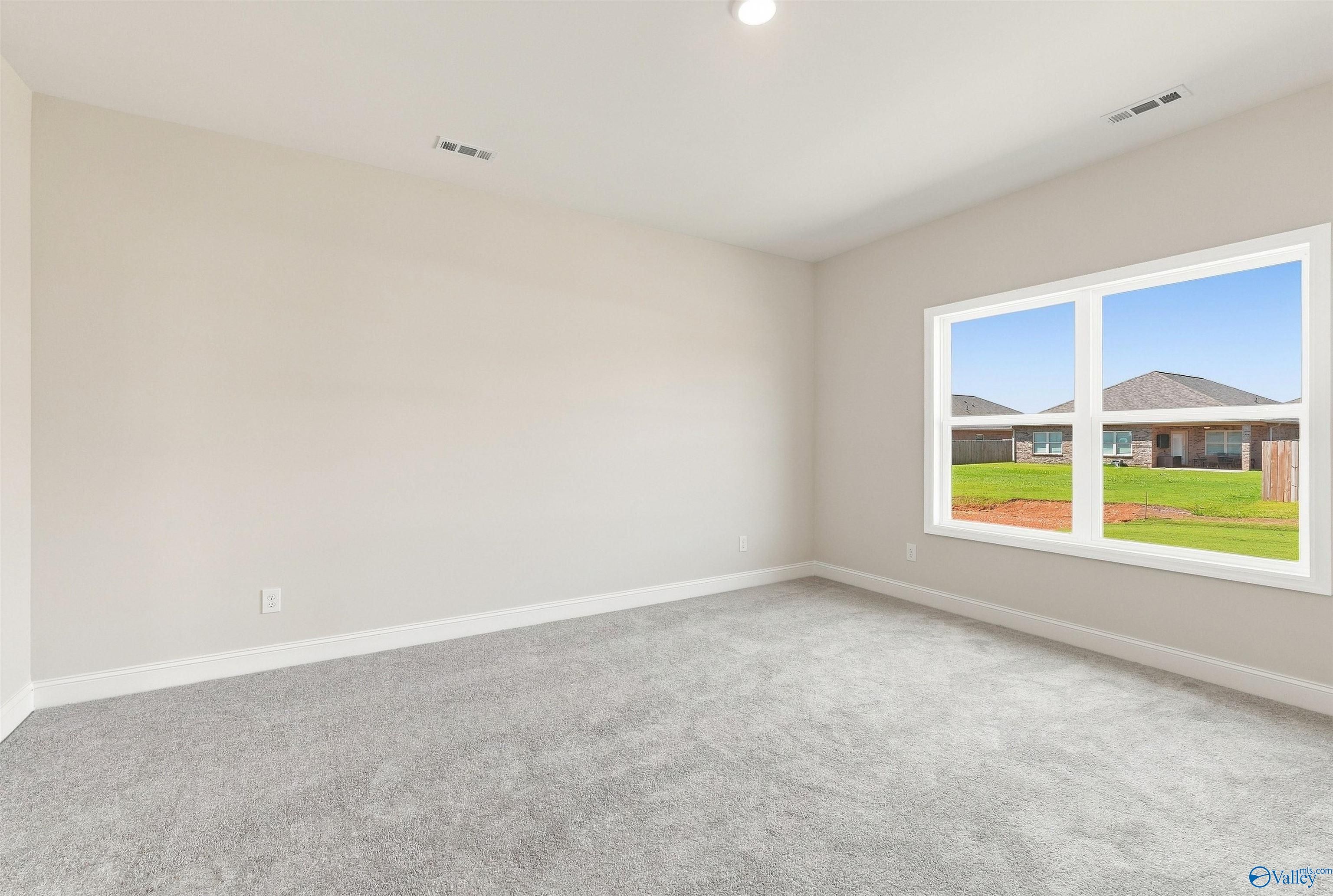 Bright empty bedroom with gray carpet and large window overlooking backyard in Davidson Homes The Everett B, Toney, Alabama