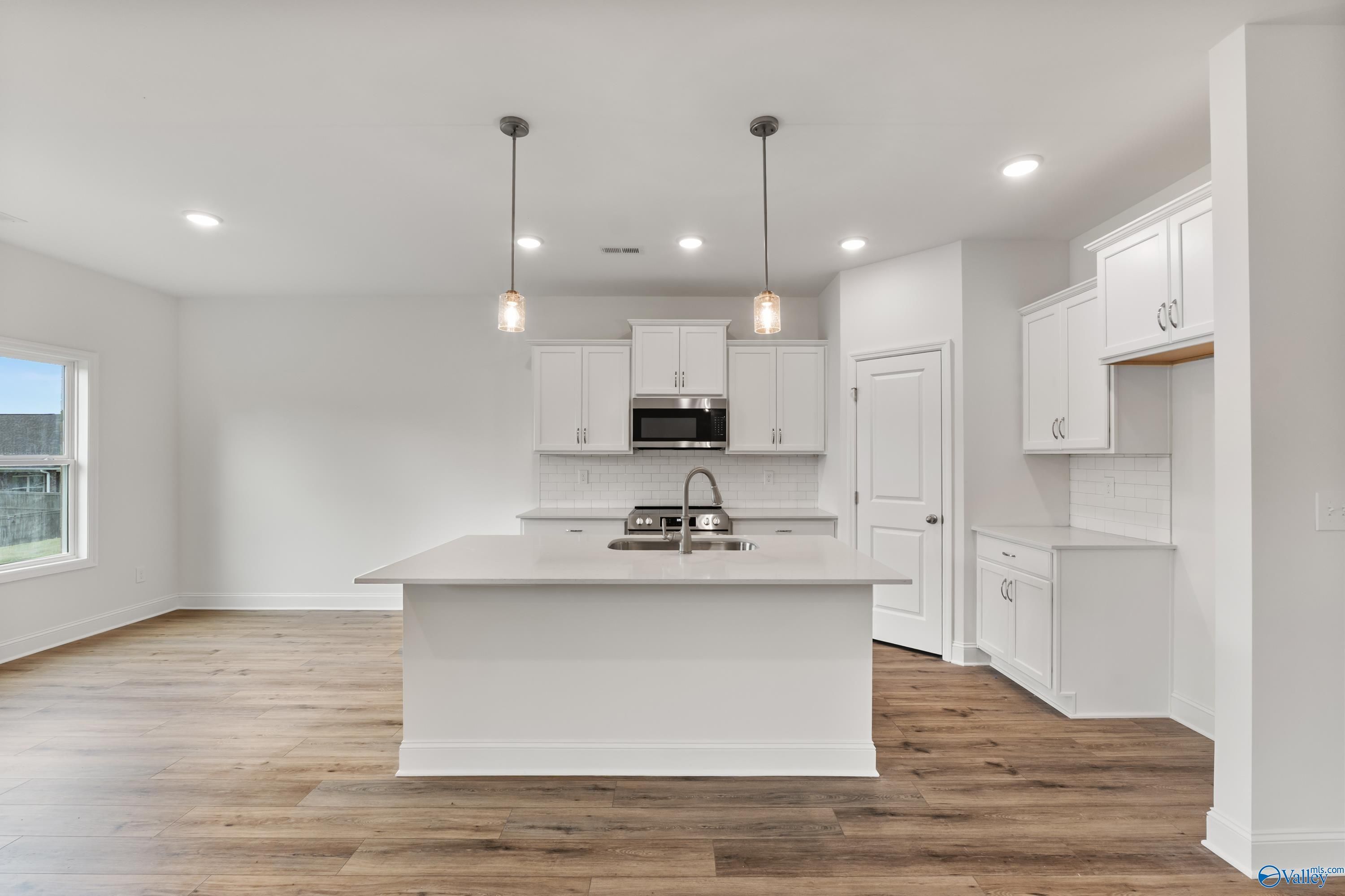 Modern white kitchen with oversized island, stainless microwave, shaker cabinets, and hardwood floors in Davidson Homes The Asheville C, New Market, AL