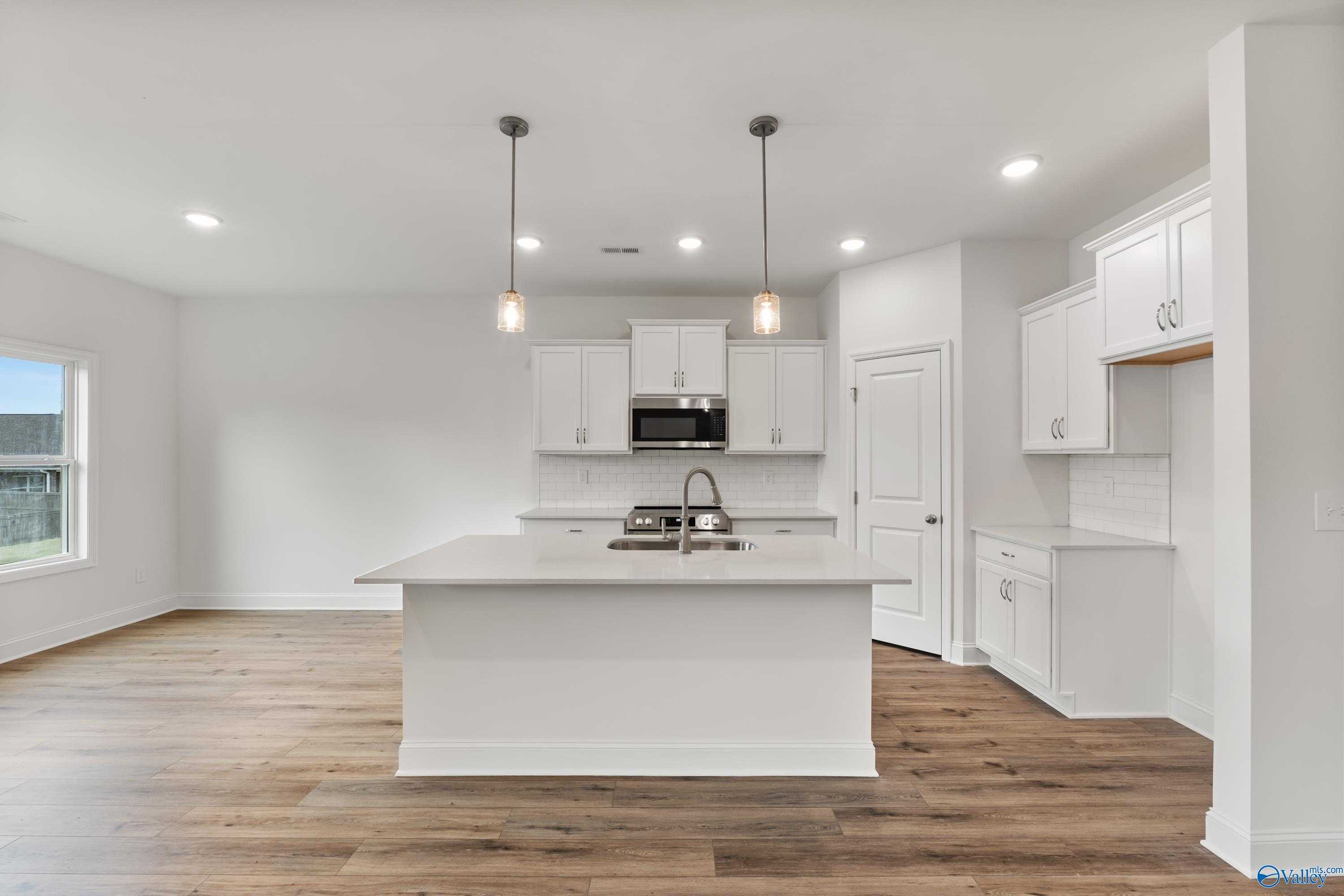 Modern white kitchen with oversized island, stainless microwave, shaker cabinets, and hardwood floors in Davidson Homes The Asheville C, New Market, AL