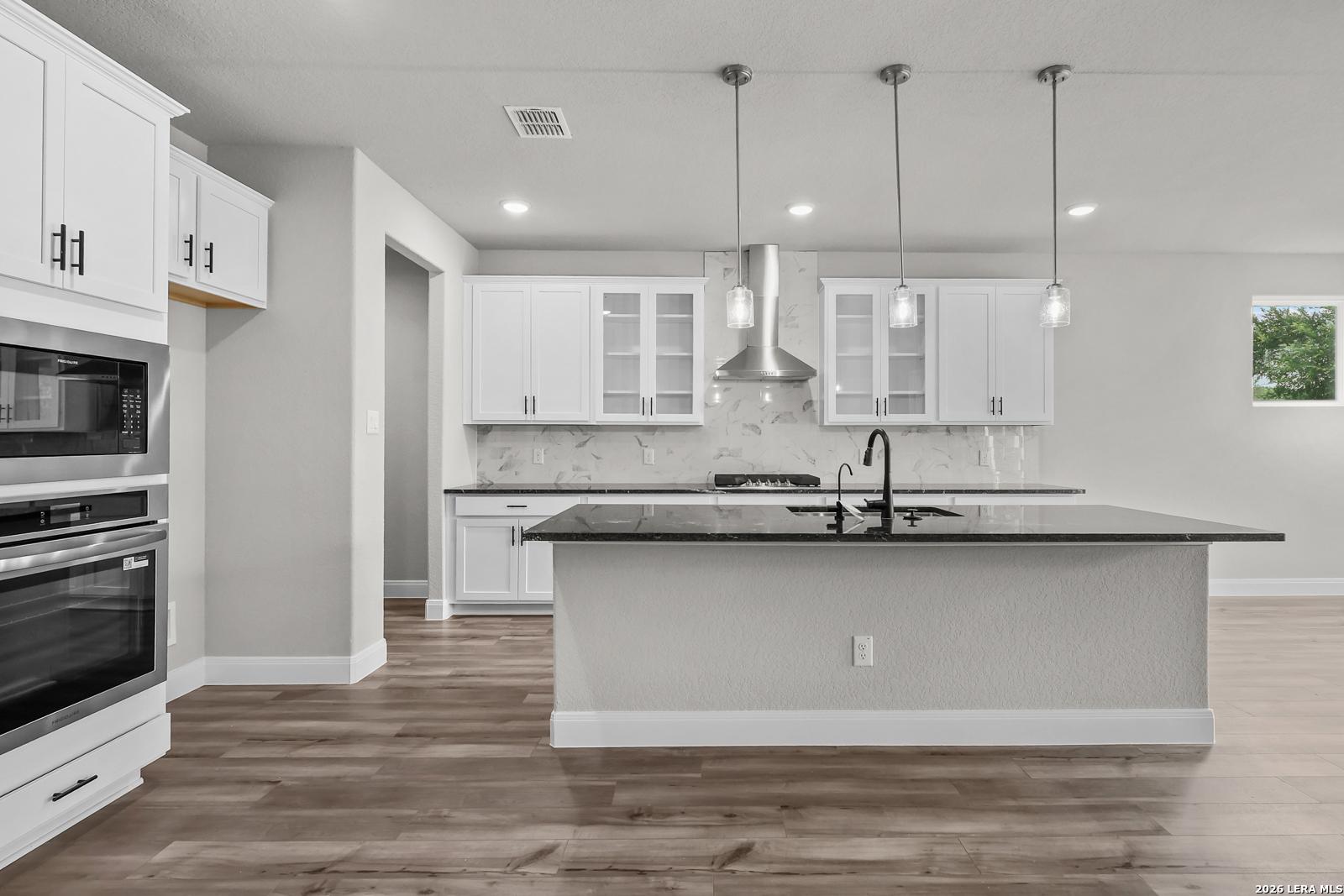 Modern white kitchen featuring black granite island, stainless steel oven and range hood, pendant lights in The Belmont H, Castroville, Texas