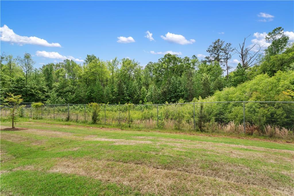 Fenced grassy backyard with lush wooded backdrop under blue sky in Summer Vineyard, Phenix City, Alabama Davidson Homes The Bartlett