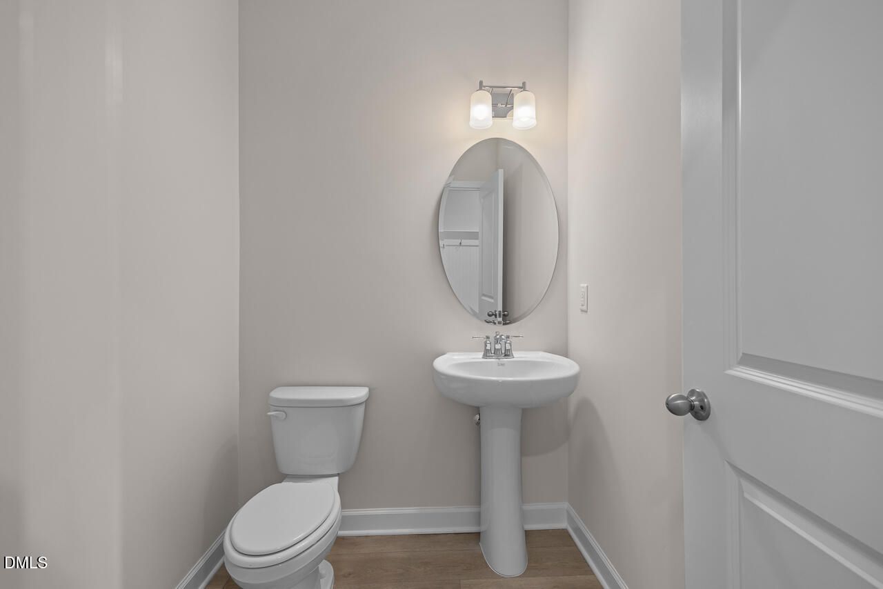 Elegant powder room featuring pedestal sink, round mirror, and toilet in Davidson Homes The Cypress D II, Angier, NC