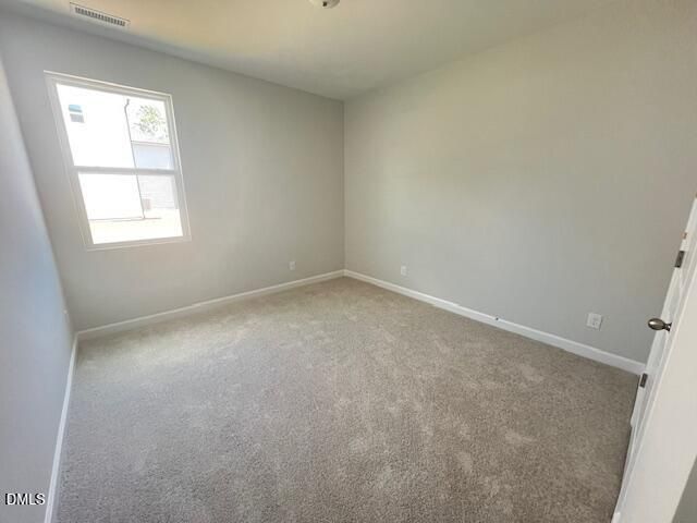 Bright empty bedroom with light gray walls, neutral carpet, and large window in Davidson Homes Adalynn A, Lillington, NC