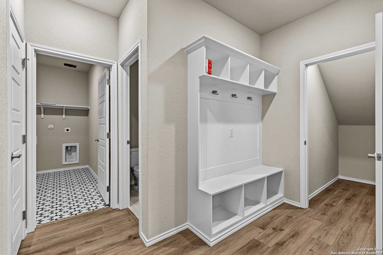 Functional mudroom with white built-in bench, cubbies, and hooks next to laundry room in Davidson Homes The Douglas F, San Antonio