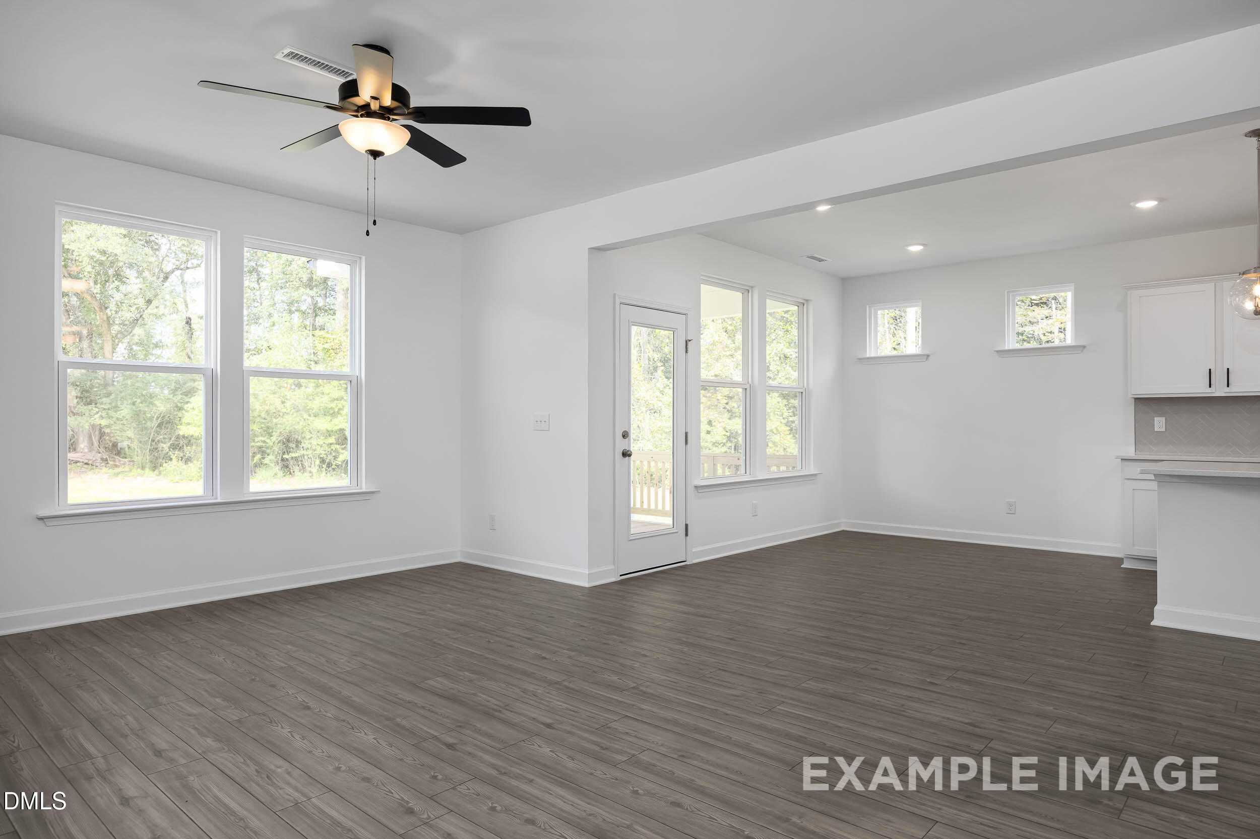 Spacious open living room with hardwood floors, ceiling fans, large windows, and French doors to patio in Davidson Homes The Willow D, Zebulon NC