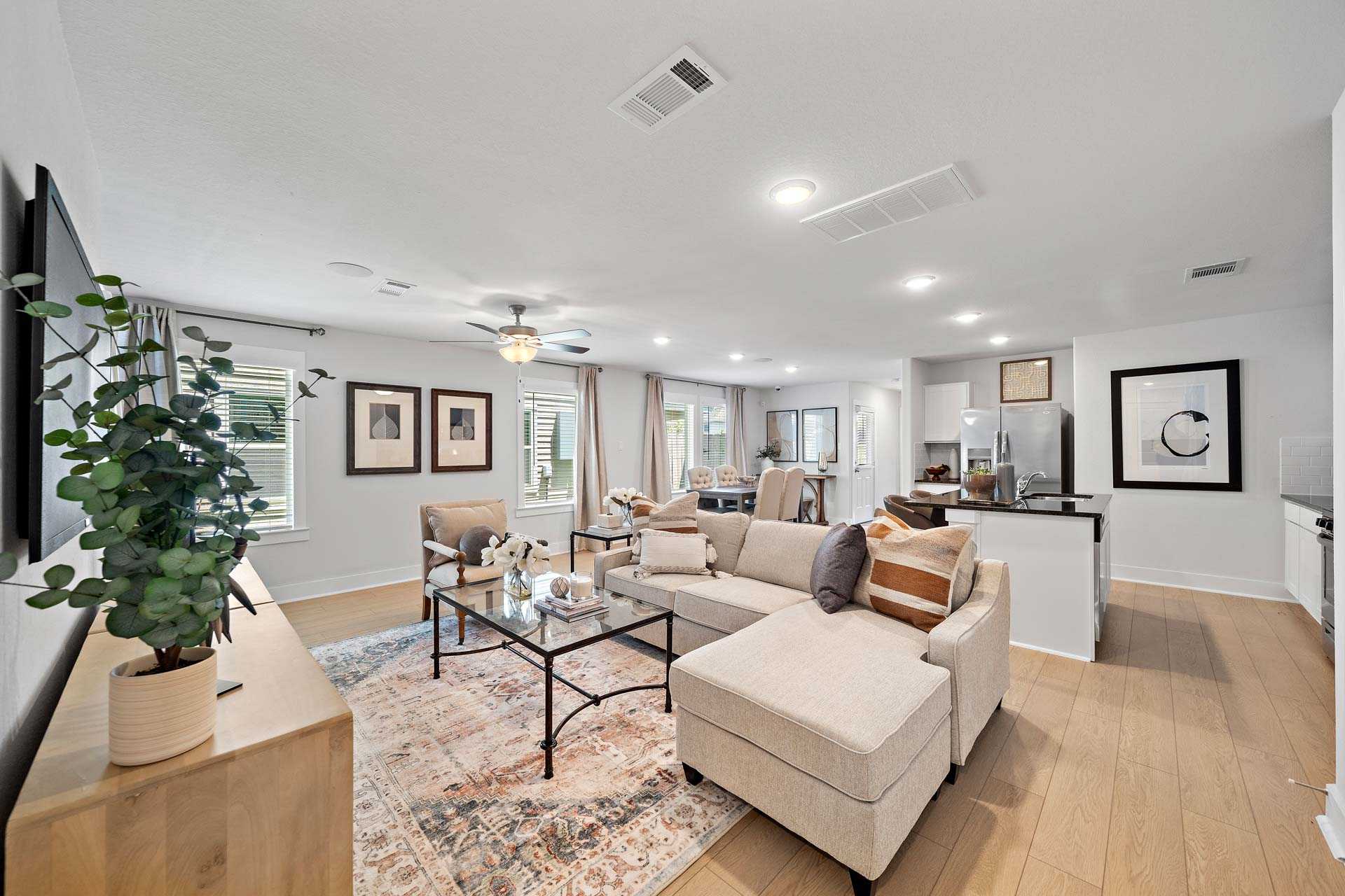 Open-concept living room and kitchen at Haven at Kieth Harrow in Cypress, Texas with hardwood floors, beige sectional sofa, and modern decor