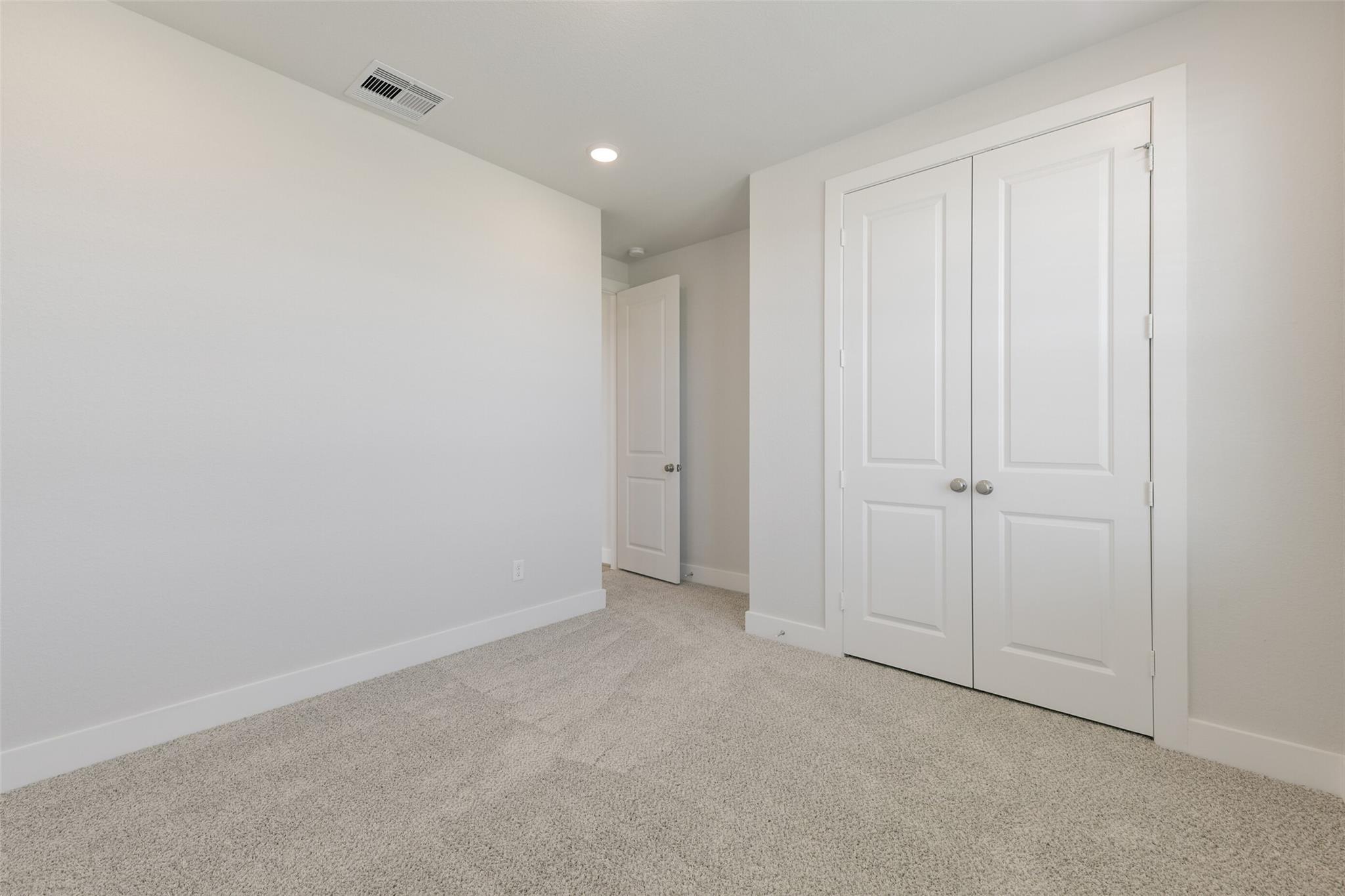 Bright secondary bedroom with white walls, beige carpet, and double closet doors in Davidson Homes The Edward A, Lago Mar, Texas City