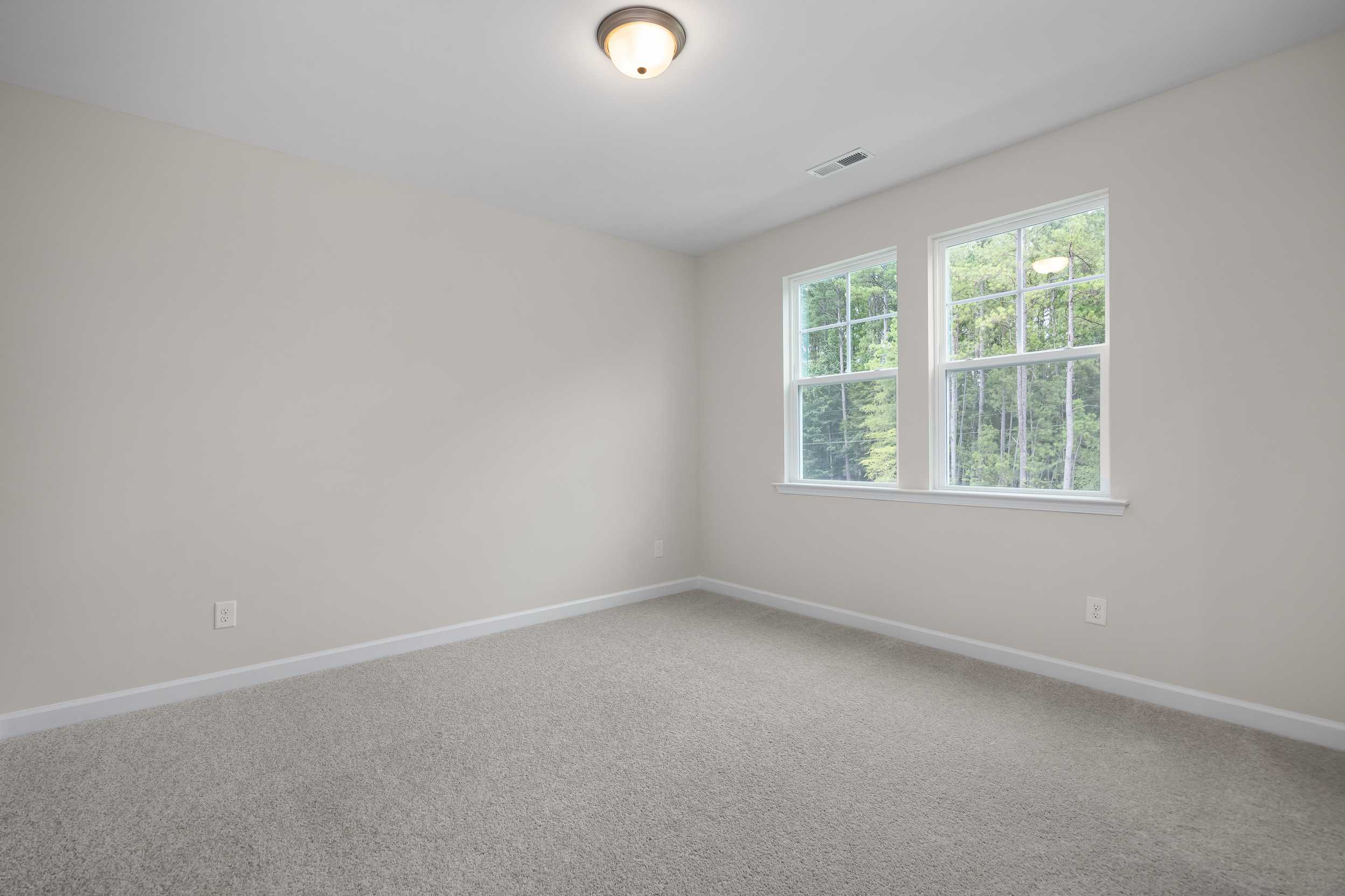 Spacious empty bedroom in The Beech C Davidson Homes design featuring large windows, neutral beige walls, and carpeted floor