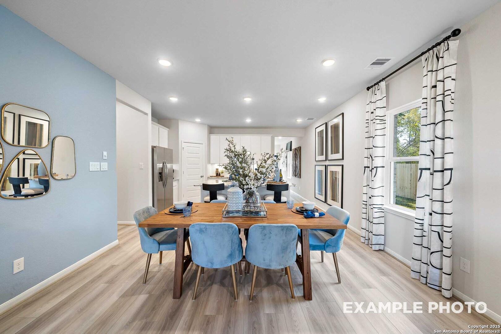 Elegant dining room featuring wooden table, blue velvet chairs, gold mirrors on blue wall, open to kitchen in Davidson Homes The San Marcos D, San Antonio