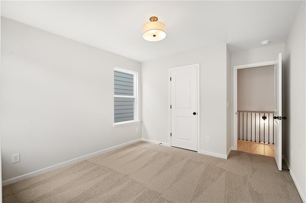 Bright upstairs bedroom with neutral walls, beige carpet, chandelier, and window in Davidson Homes The Marion A, Kennesaw, GA
