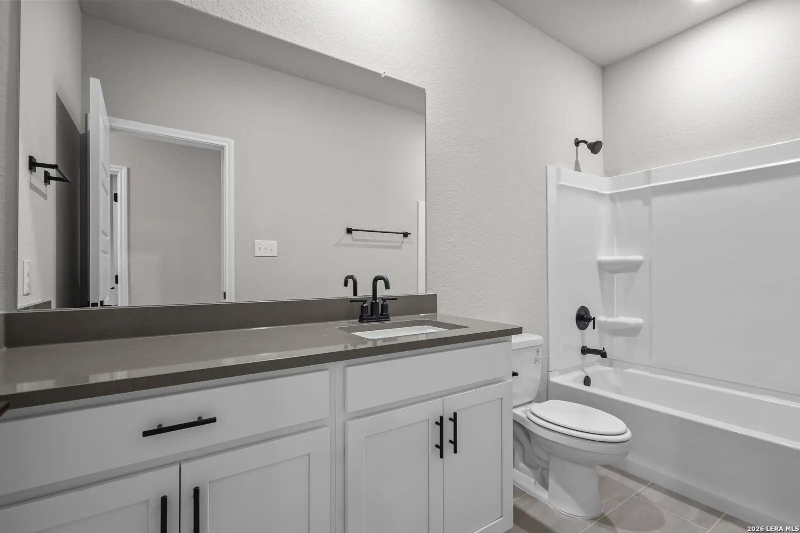 Modern bathroom with white vanity, dark hardware, and shower-tub combo in The Glenwood E floor plan, Comanche Ridge, TX.