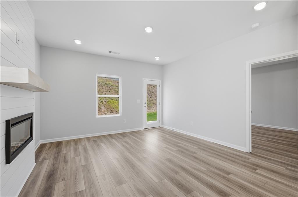 Bright great room with shiplap fireplace, wood-look flooring, and rear door in Davidson Homes' Oconee B plan, The Bluffs, Canton, GA