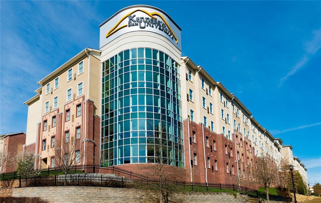 Multi-story Kensington apartments with curved glass atrium, beige and brick facade, landscaped hill setting in Kennesaw, Georgia