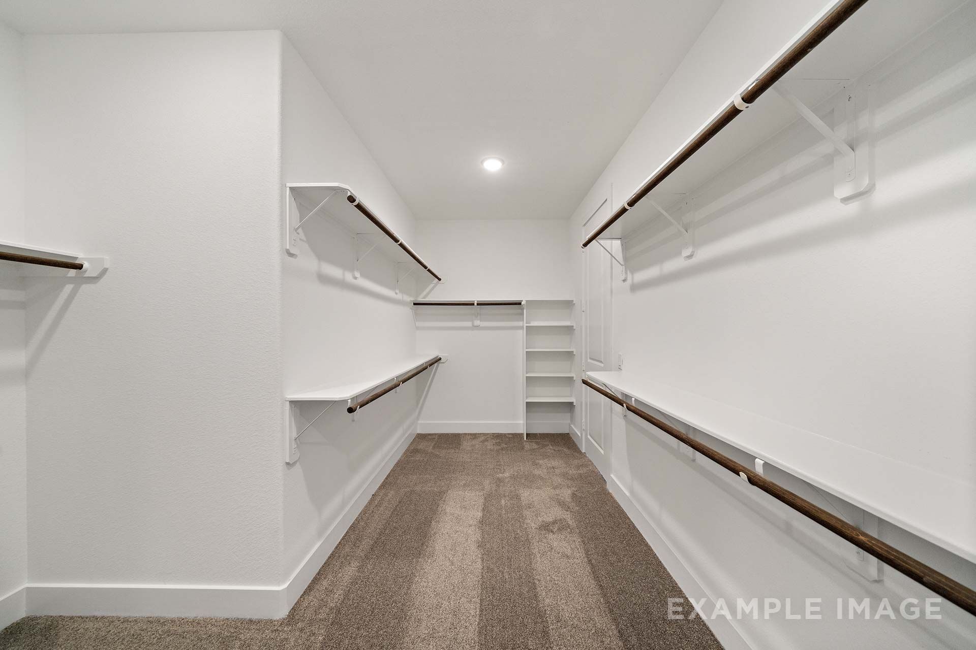 Spacious walk-in master closet in The Victoria by Davidson Homes, featuring white shelving, wood hanging rods, and carpet.