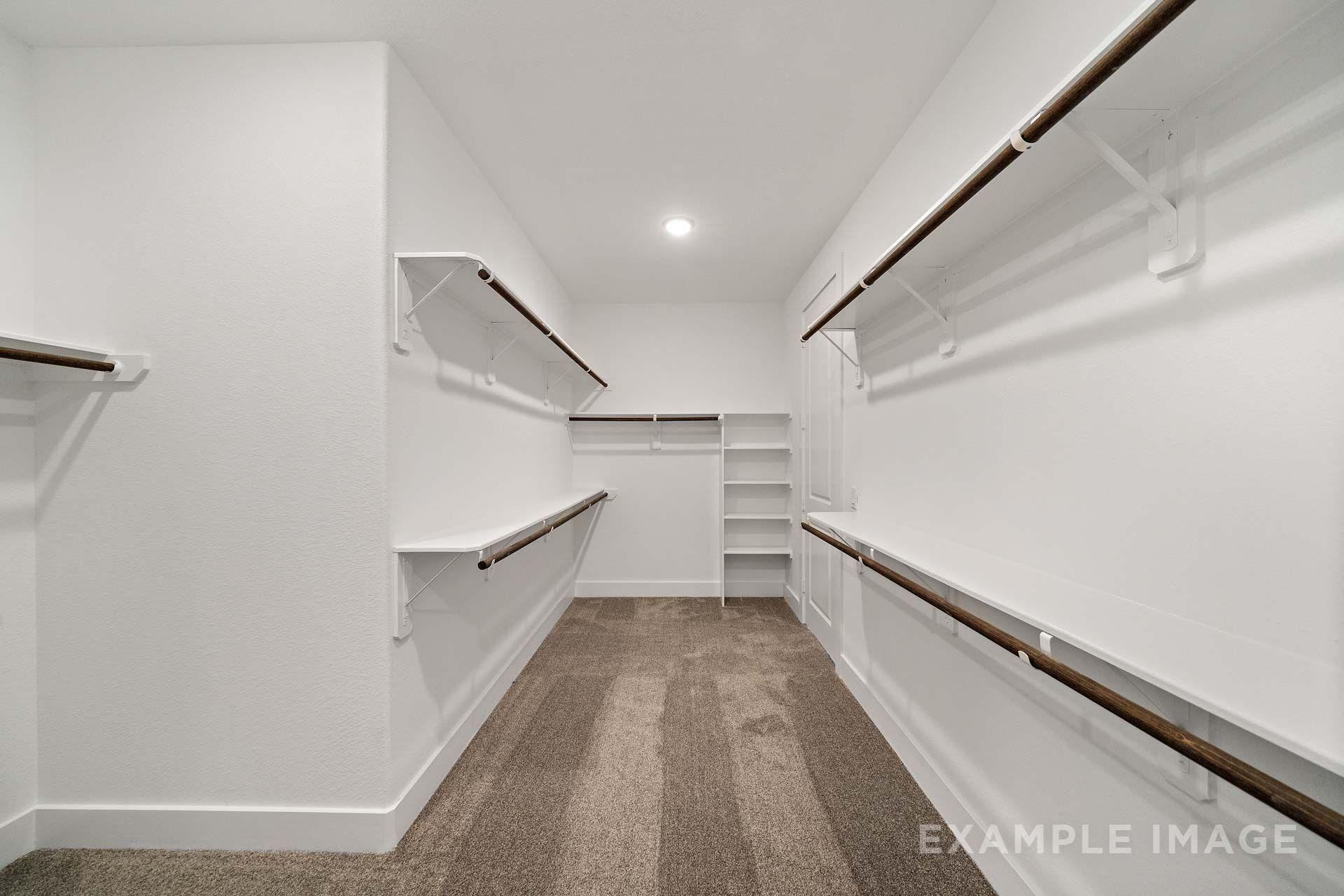Spacious walk-in master closet in The Victoria by Davidson Homes, featuring white shelving, wood hanging rods, and carpet.