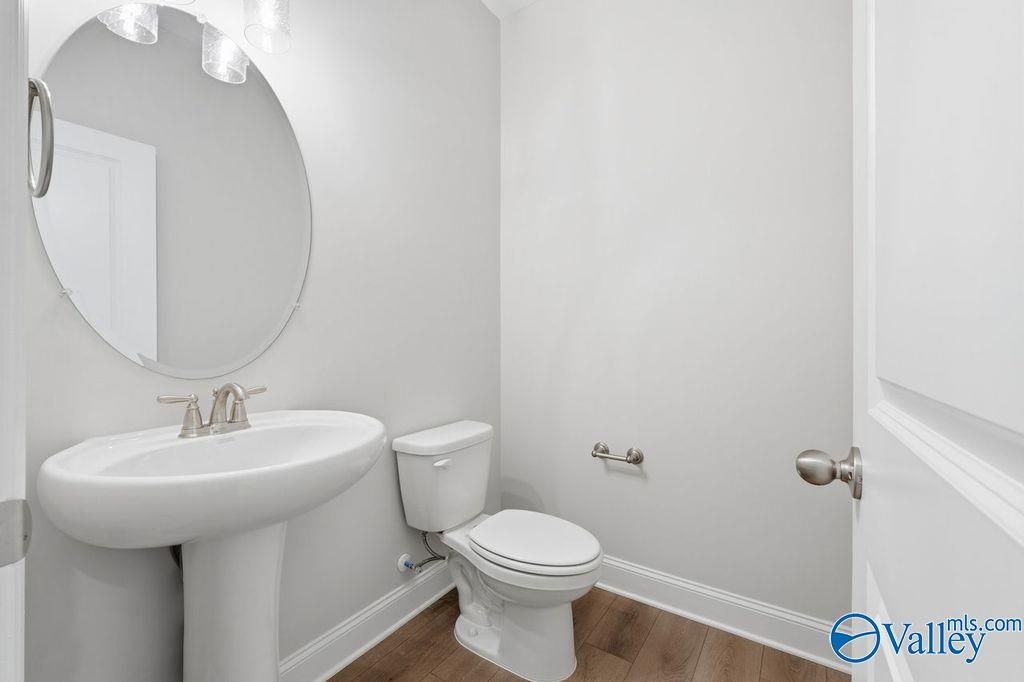 Elegant powder room with round mirror, white pedestal sink, toilet, gray walls in Davidson Homes The Harrison, Hartselle, AL