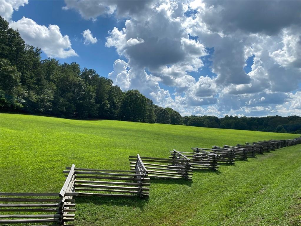 Scenic split-rail wooden fence along lush green pasture and wooded backdrop under partly cloudy sky in The Village at Shallowford, Kennesaw, Georgia