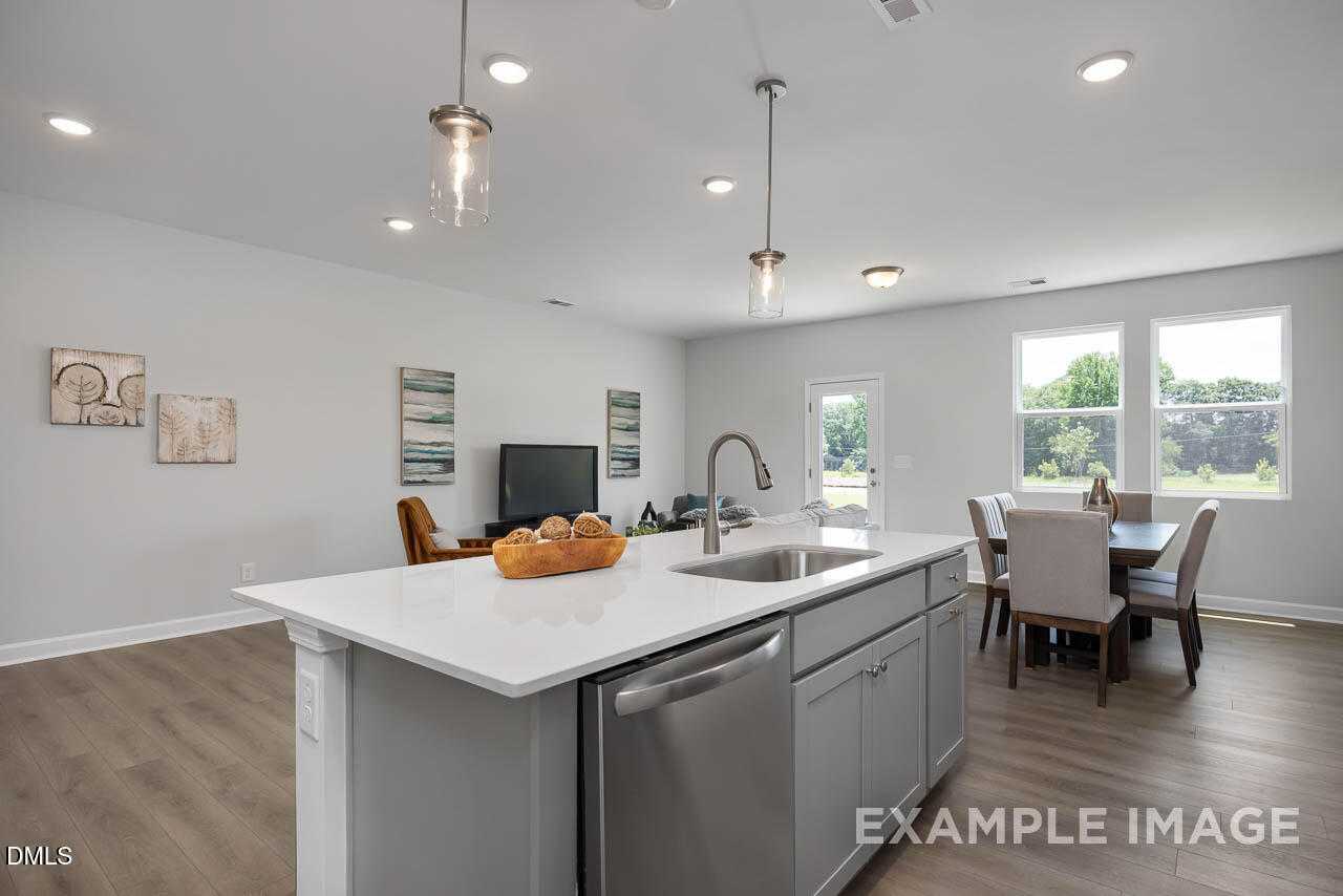 Modern open-concept kitchen with white island, stainless dishwasher, and dining area in Davidson Homes The Warren, Fuquay-Varina, NC