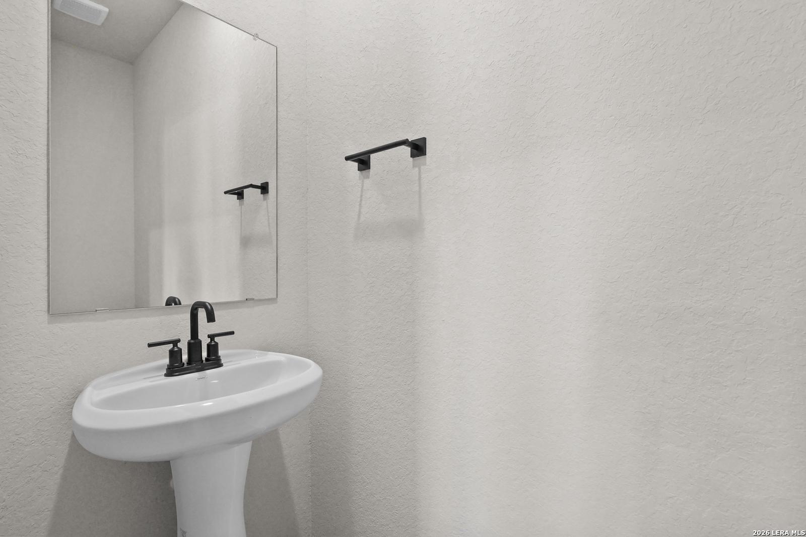 White pedestal sink with matte black faucet and mirror in half bath at Davidson Homes The Glenwood E, Comanche Ridge, San Antonio