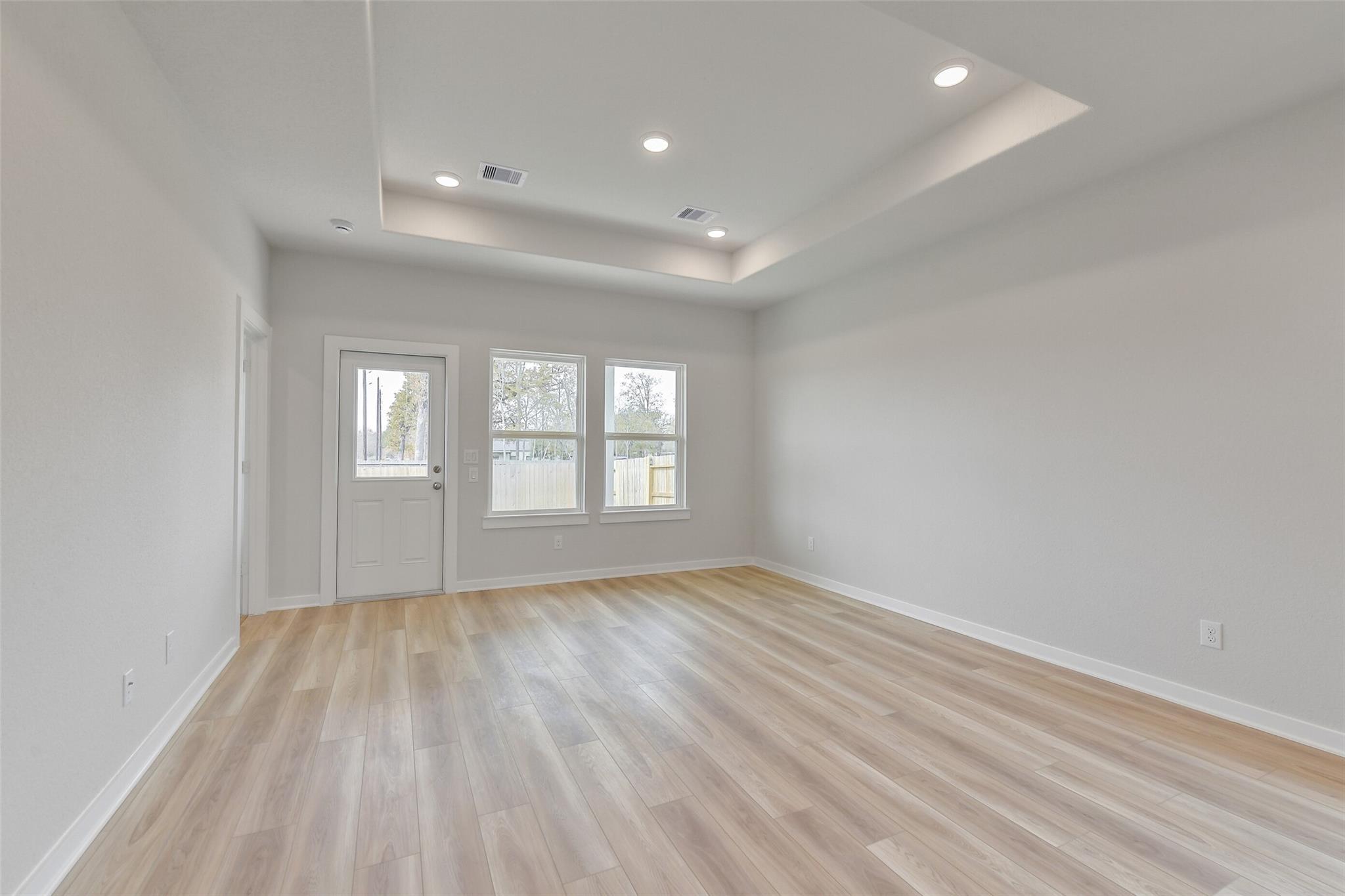 Bright living area with tray ceiling and wood-look flooring in The Colorado G floor plan at Windmill Estates, Magnolia.