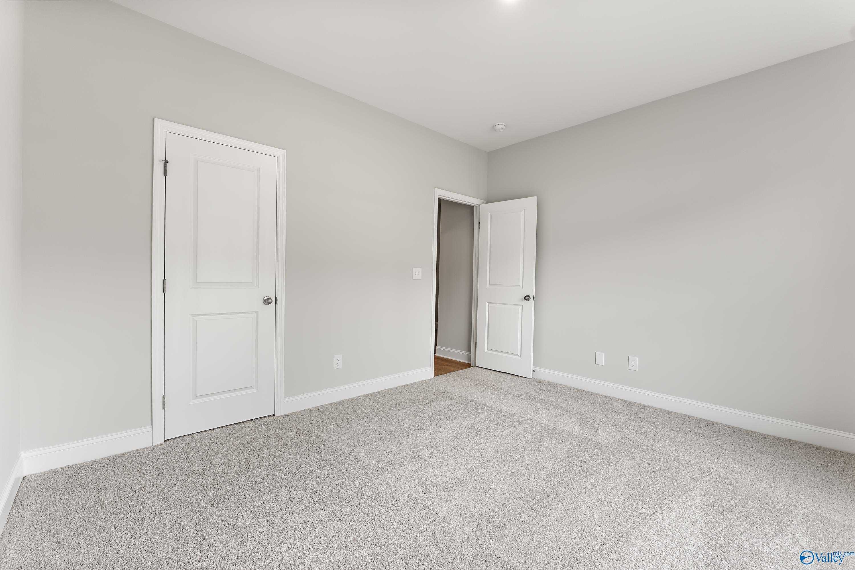 Spacious empty bedroom with light gray walls, white doors, and plush carpet in Davidson Homes The Daphne C, Athens, Alabama
