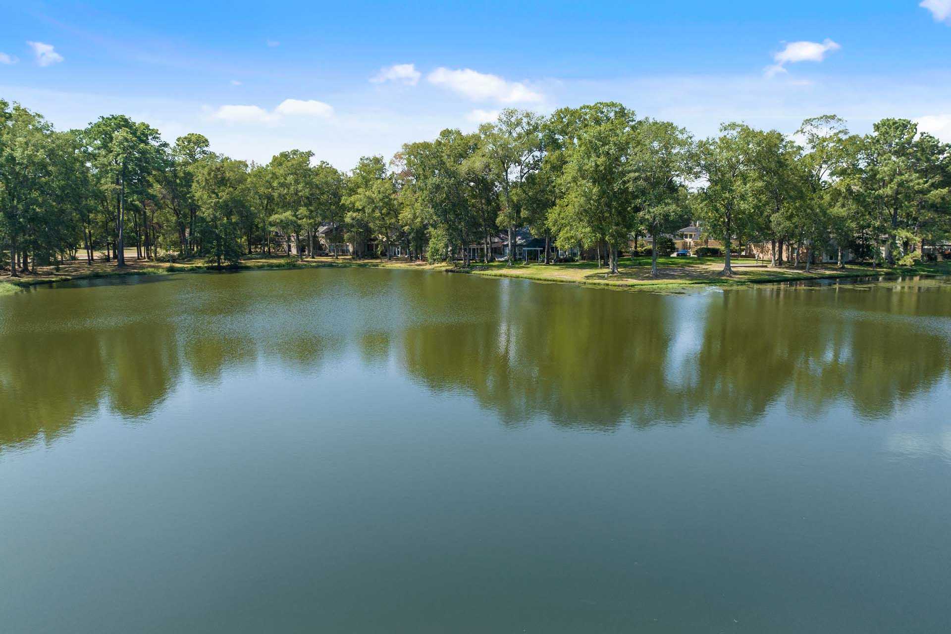 Tree-lined pond with calm reflections and distant homes at Enclave at Newport in Crosby Texas