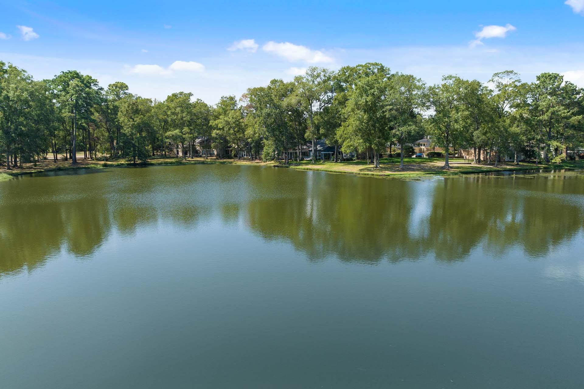 Tree-lined pond with calm reflections and distant homes at Enclave at Newport in Crosby Texas