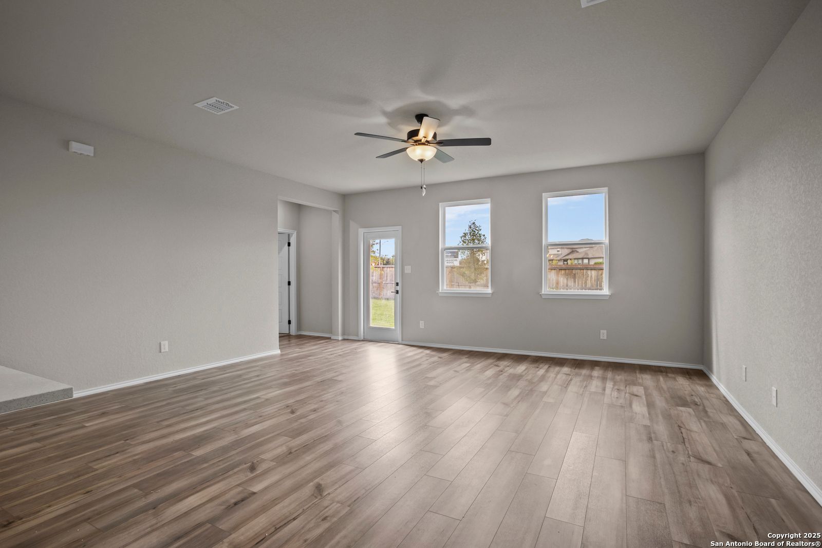 Bright living room with hardwood floors, ceiling fan, and French doors to backyard in Davidson Homes The Douglas F, San Antonio