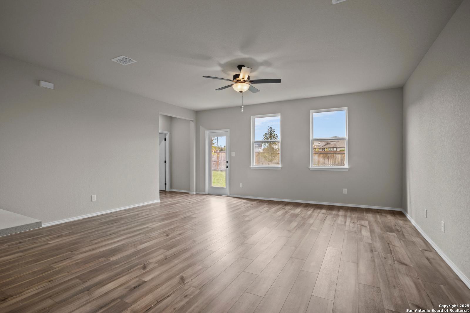 Bright living room with hardwood floors, ceiling fan, and French doors to backyard in Davidson Homes The Douglas F, San Antonio