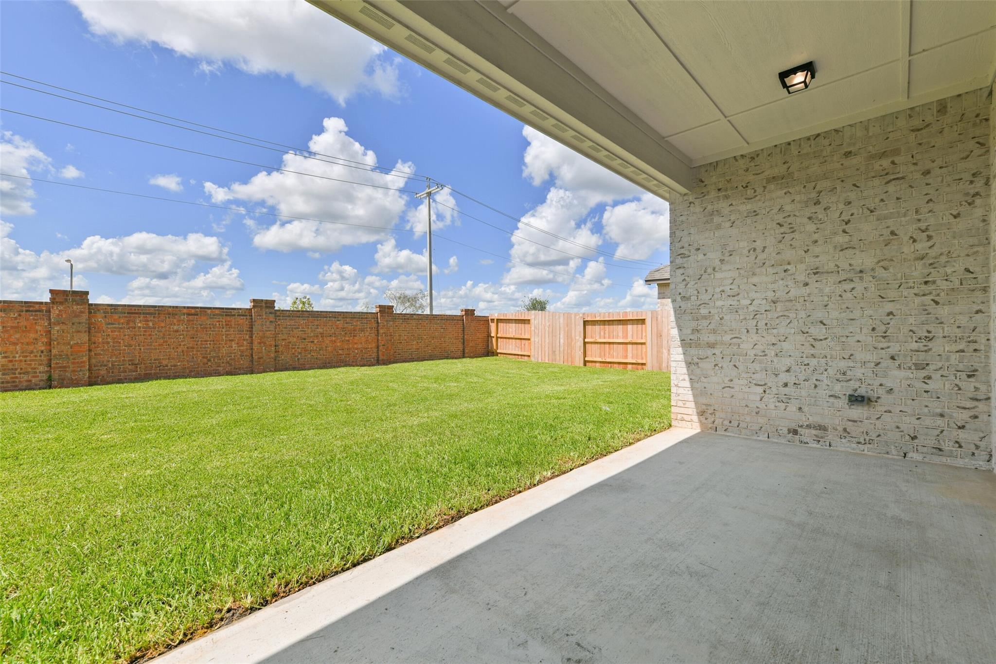Covered patio overlooking lush green backyard with brick fencing in Davidson Homes The Edward A, Lago Mar, Texas City