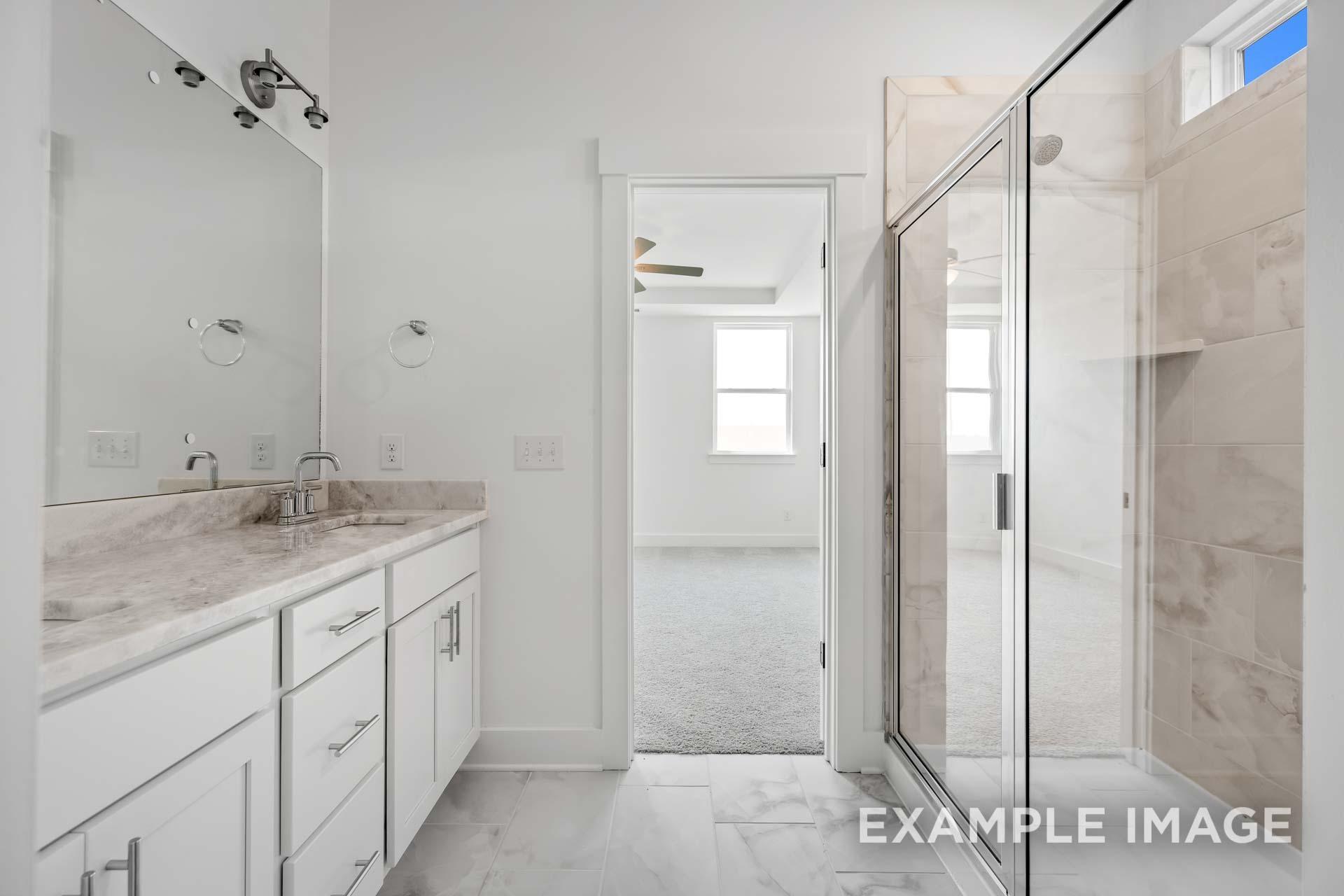 Spacious master bathroom in The Ash C featuring white cabinetry, marble vanity, frameless glass shower, and bedroom view