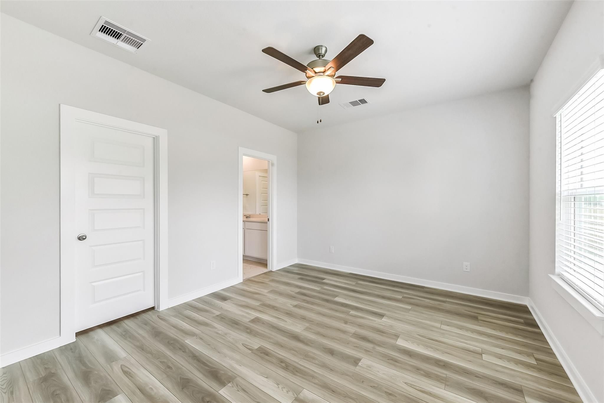 Bright bedroom with ceiling fan, attached bath, luxury vinyl plank floors in Davidson Homes The Frio G, Magnolia, Texas