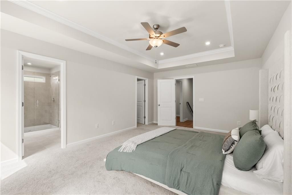 Master bedroom with tray ceiling, ceiling fan, green bedding, en-suite shower, and walk-in closet in Davidson Homes The Marion B, Kennesaw, GA