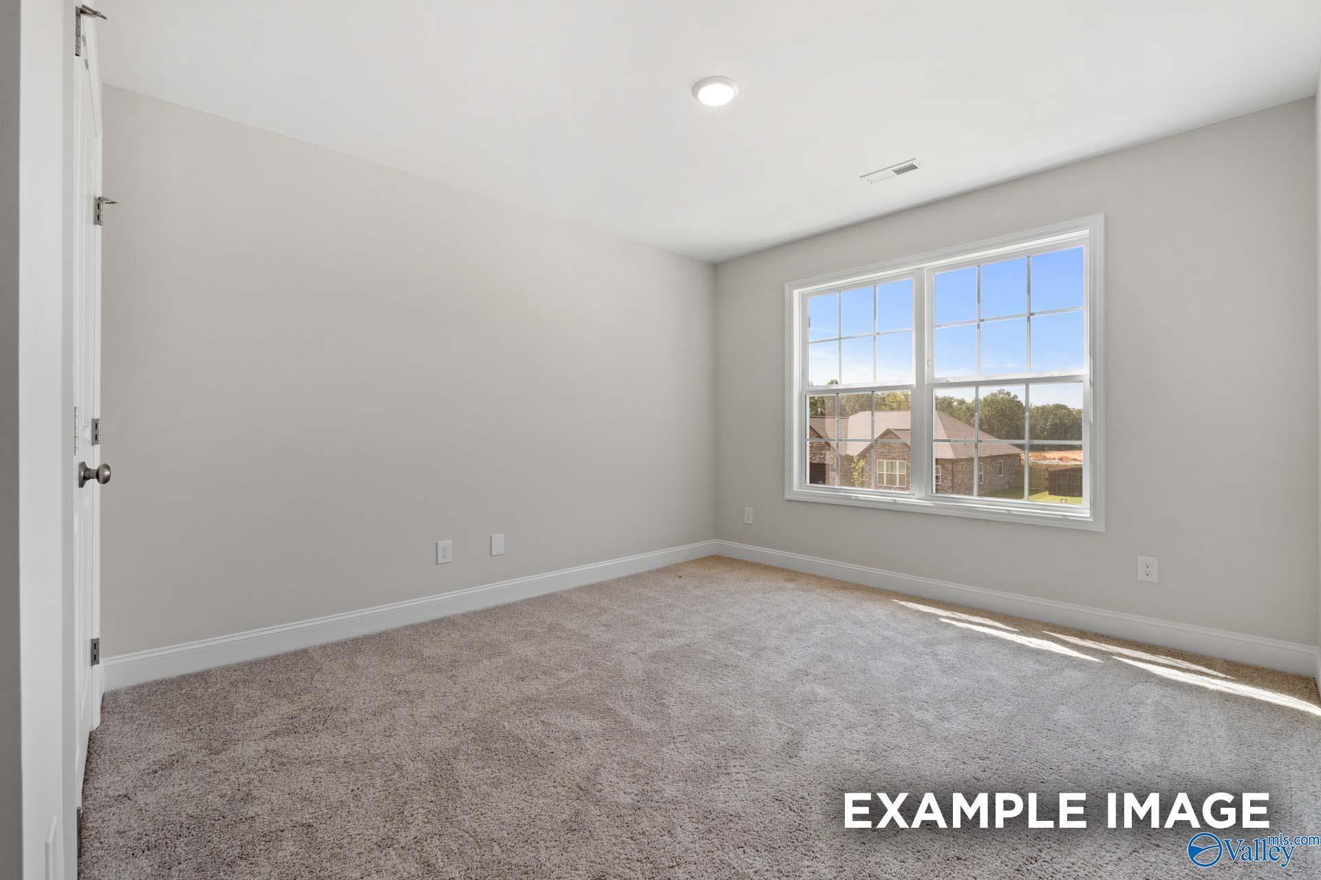 Empty bedroom with light gray walls, beige carpeted floor, and large window overlooking neighborhood in Davidson Homes Madison A, Meridianville AL