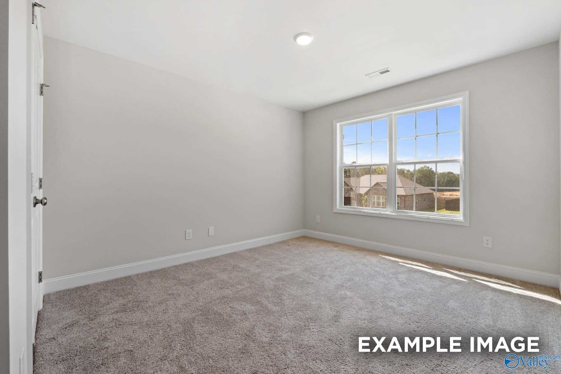 Bright secondary bedroom with gray walls, beige carpet, and large sunny window in Davidson Homes The Madison A, Meridianville, Alabama