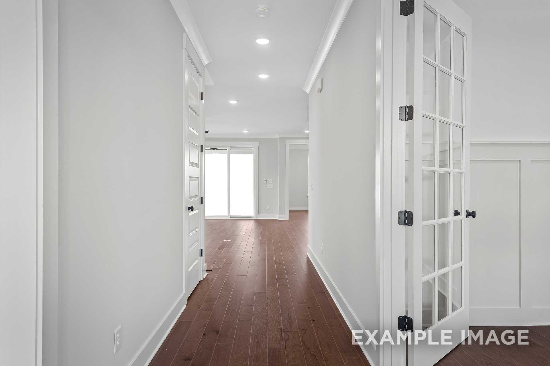 Spacious hallway in The Hathaway home with white walls, hardwood floors, French doors, and recessed lighting