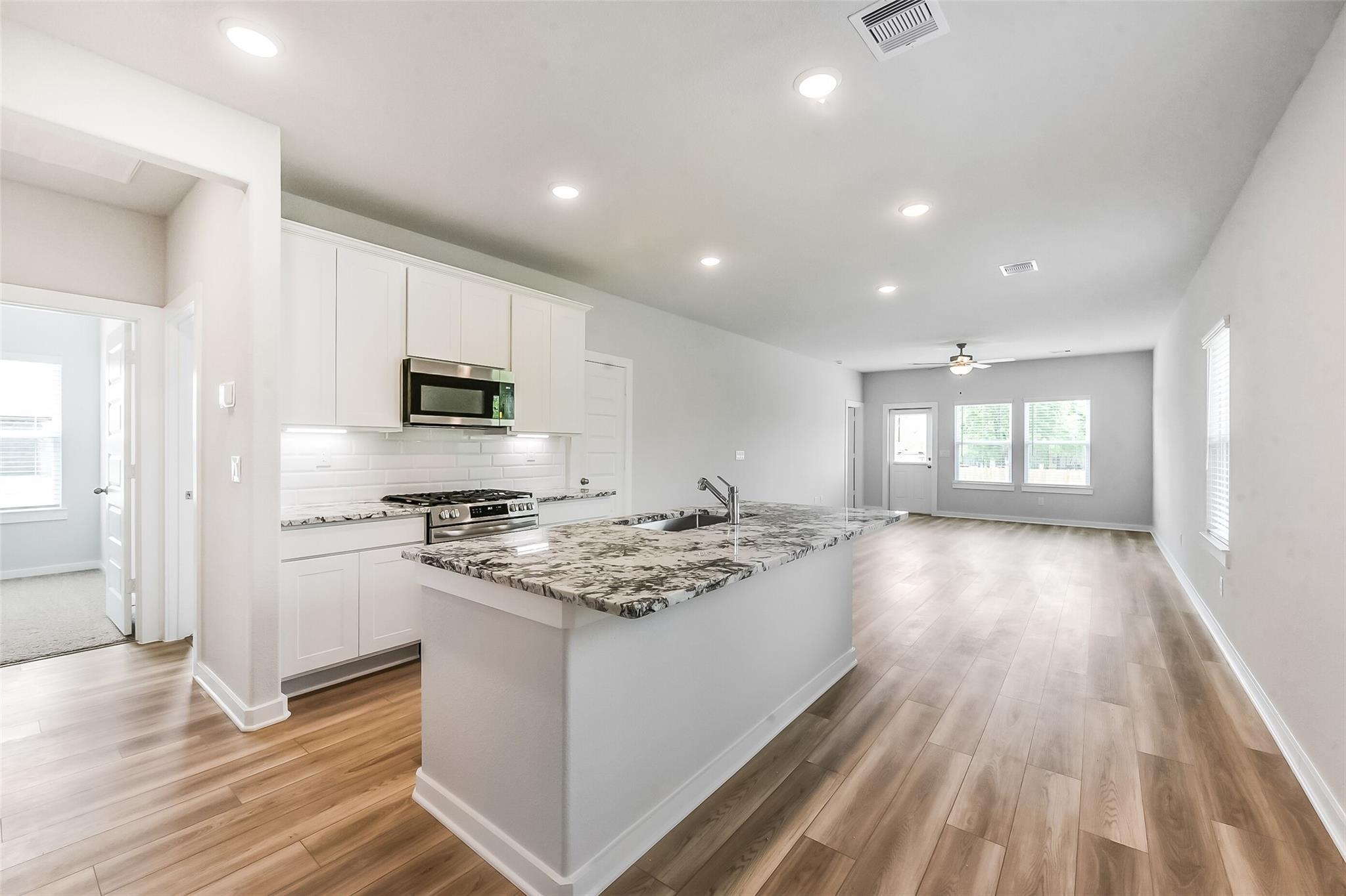 Open-concept kitchen with white cabinets, granite island, stainless appliances in Davidson Homes The Frio G, Magnolia, Texas
