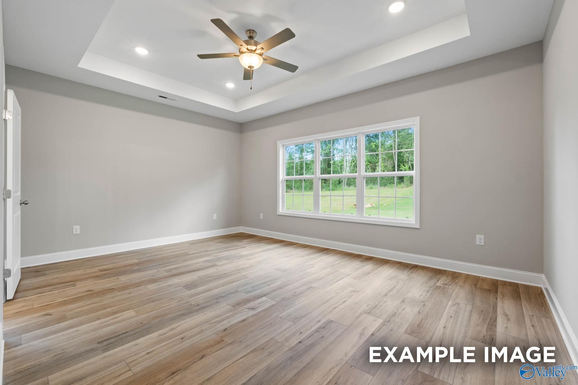 Bright bedroom with tray ceiling, ceiling fan, large windows to wooded view, light oak hardwood floors in Davidson Homes The Montgomery, Meridianville AL
