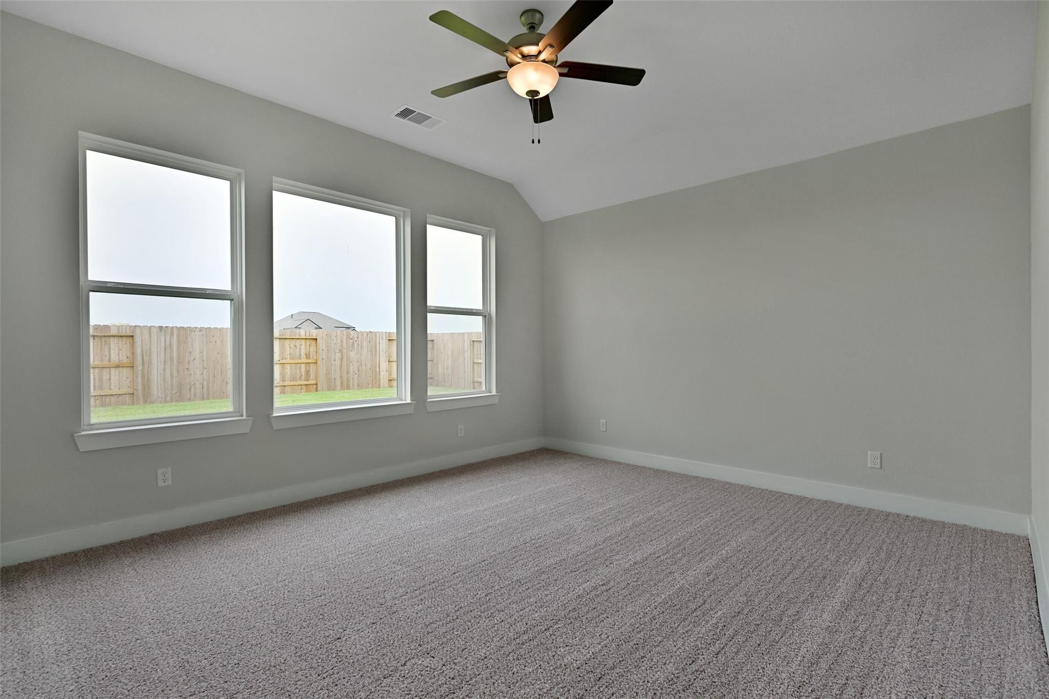 Bright bedroom with light gray walls, three large windows, ceiling fan, and backyard view in Davidson Homes The Edward A, Lago Mar, Texas City