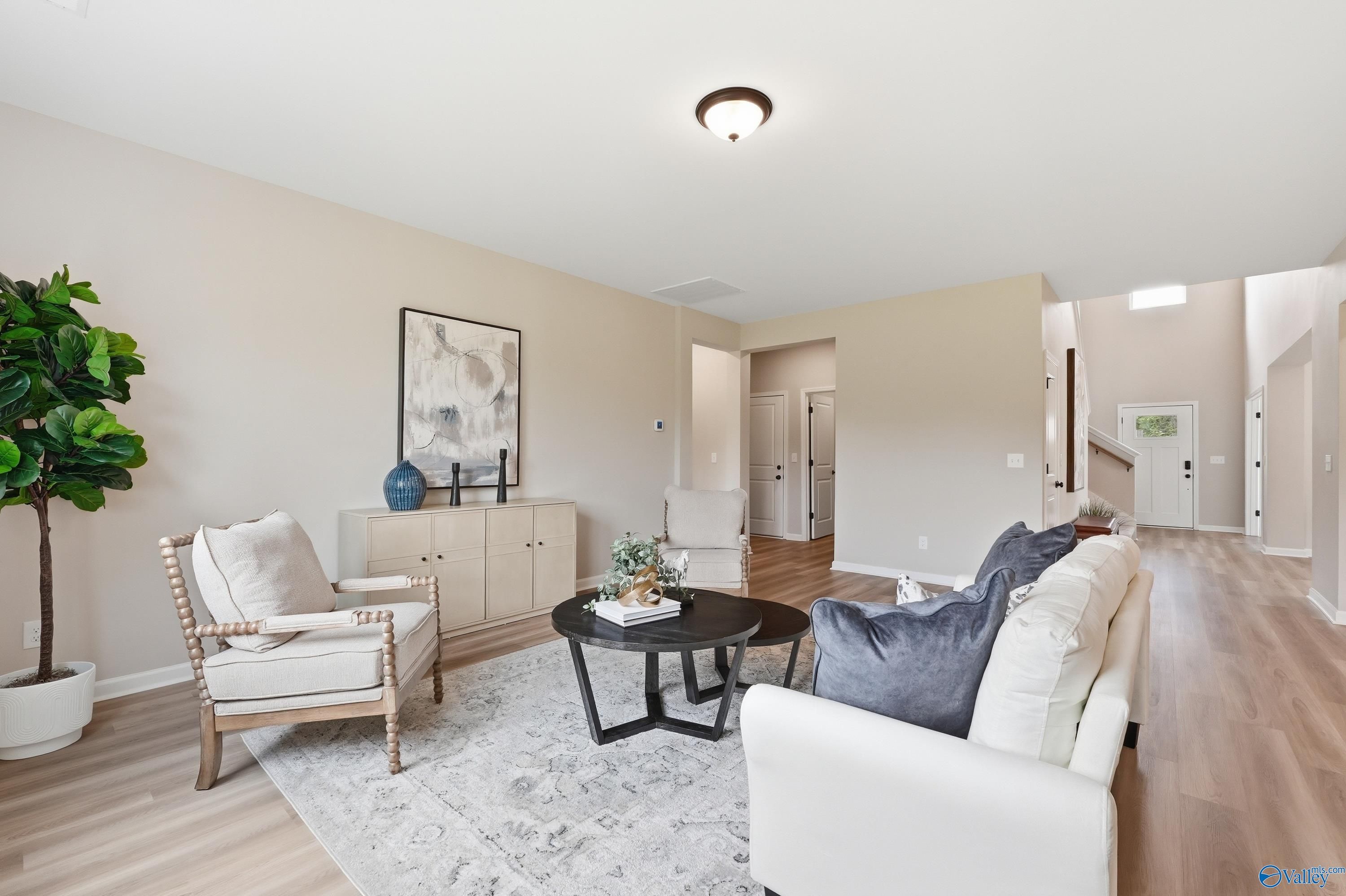 Cozy living room with white sofa, beige armchairs, fiddle leaf fig, abstract art, hardwood floors in Davidson Homes The Dorado, Huntsville