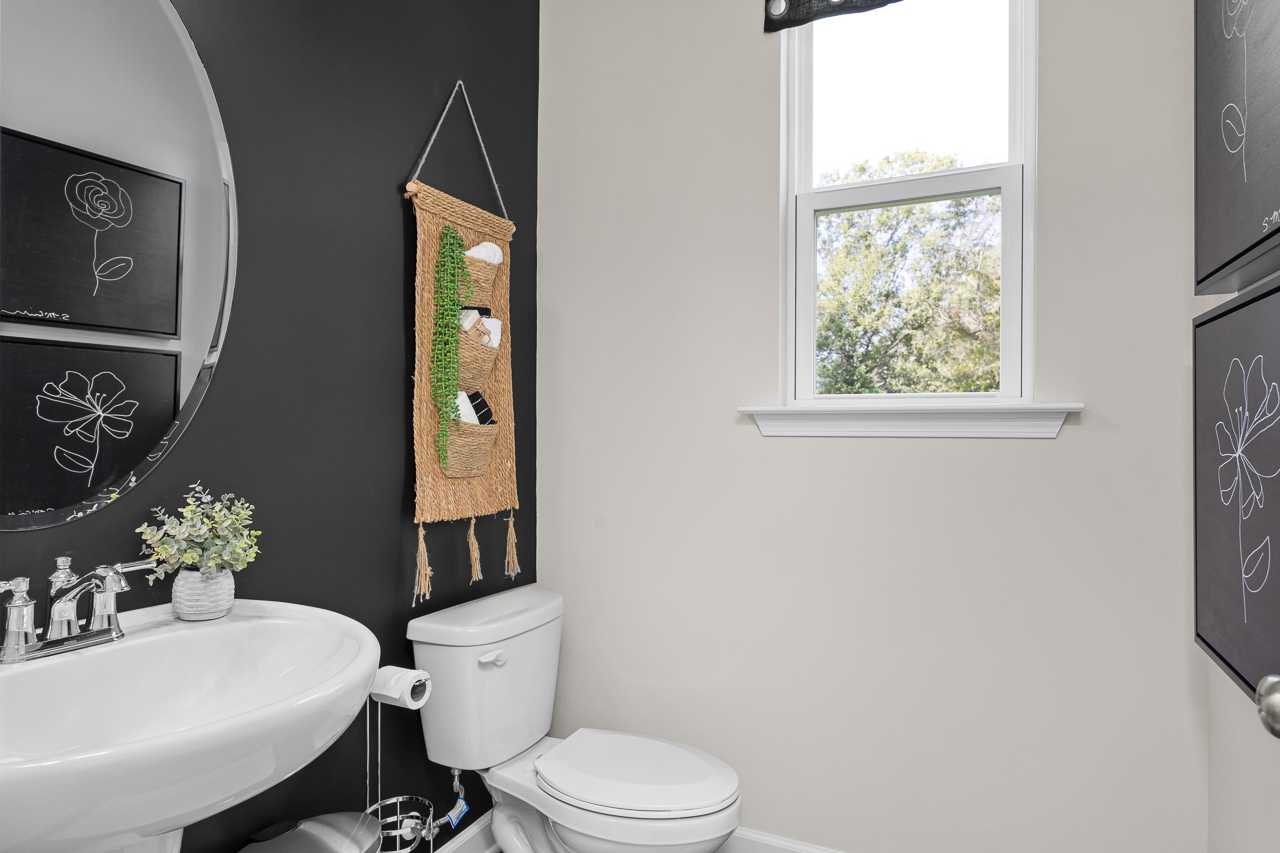 Cozy powder room at Wellers Knoll in Lillington NC with navy accent wall, round black mirror, macrame plant hanger, white vanity sink, and window view