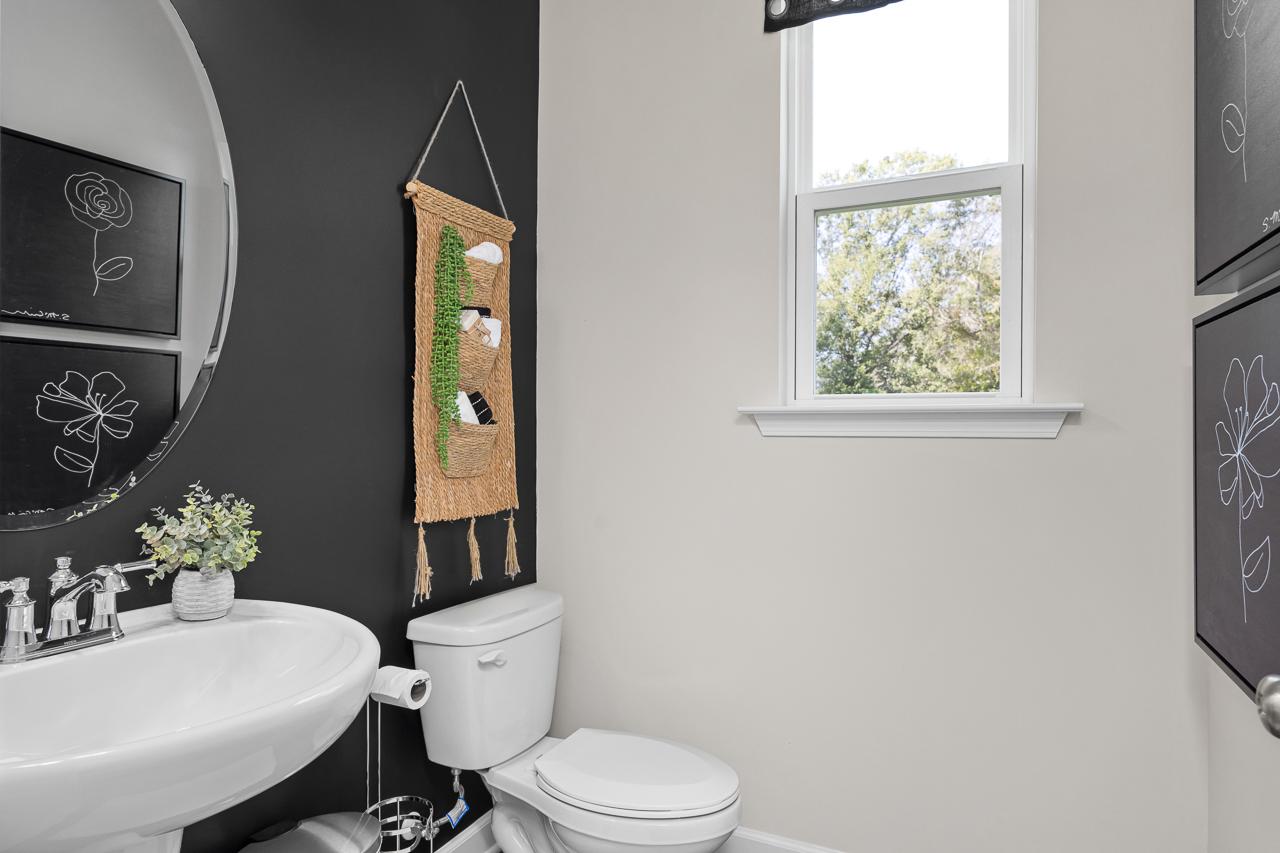 Cozy powder room at Wellers Knoll in Lillington NC with navy accent wall, round black mirror, macrame plant hanger, white vanity sink, and window view