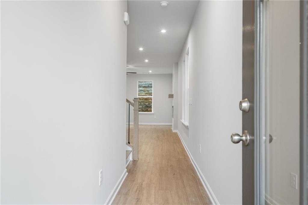 Bright hallway with oak hardwood floors, white walls, stairs, and seascape art in Davidson Homes The Cary A, Kennesaw, GA