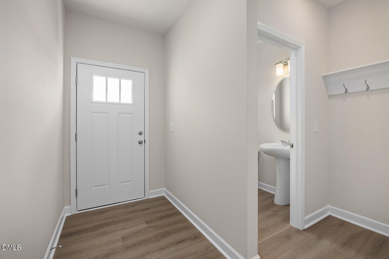 Bright entryway with white paneled door and adjacent powder room featuring round mirror, pedestal sink in The Graham Interior, Fuquay-Varina