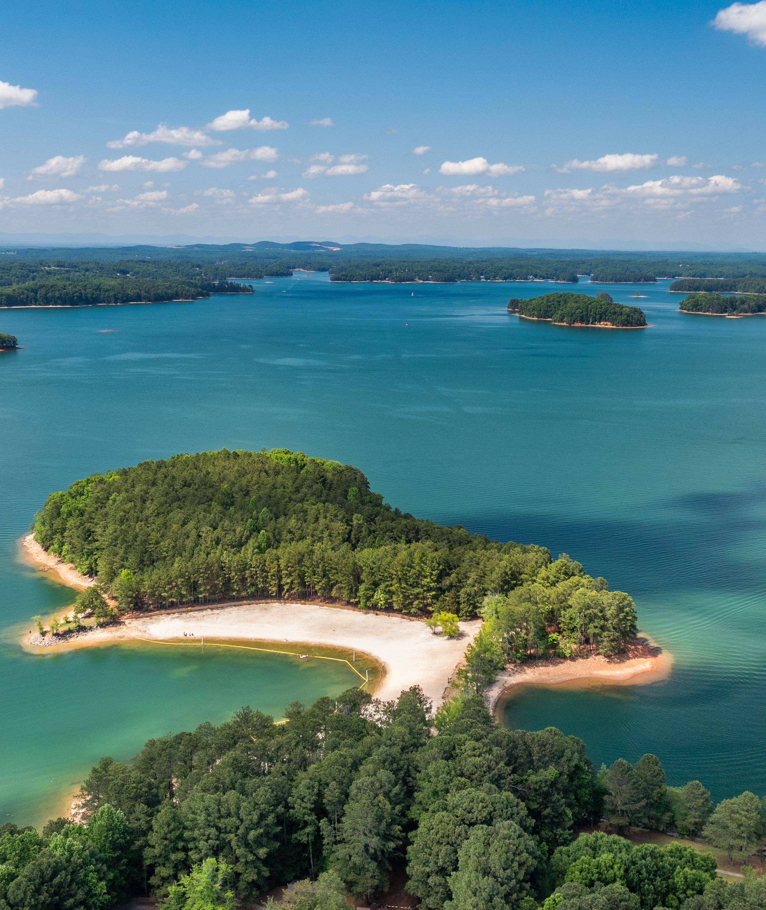 Aerial view of Lake Lanier near Lake Hollow community in Gainesville, Georgia, featuring sandy beach, wooded islands, and turquoise waters