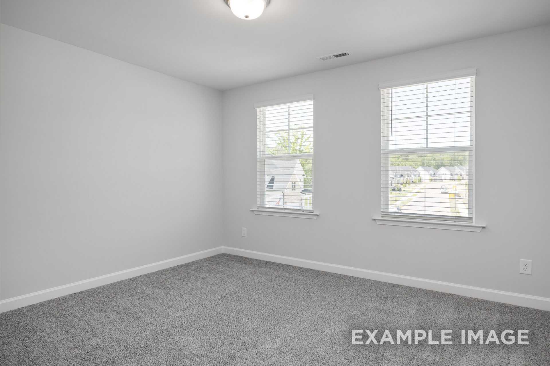 Spacious upstairs bedroom in The Preston B with gray carpet, white walls, dual large windows with blinds overlooking neighborhood homes