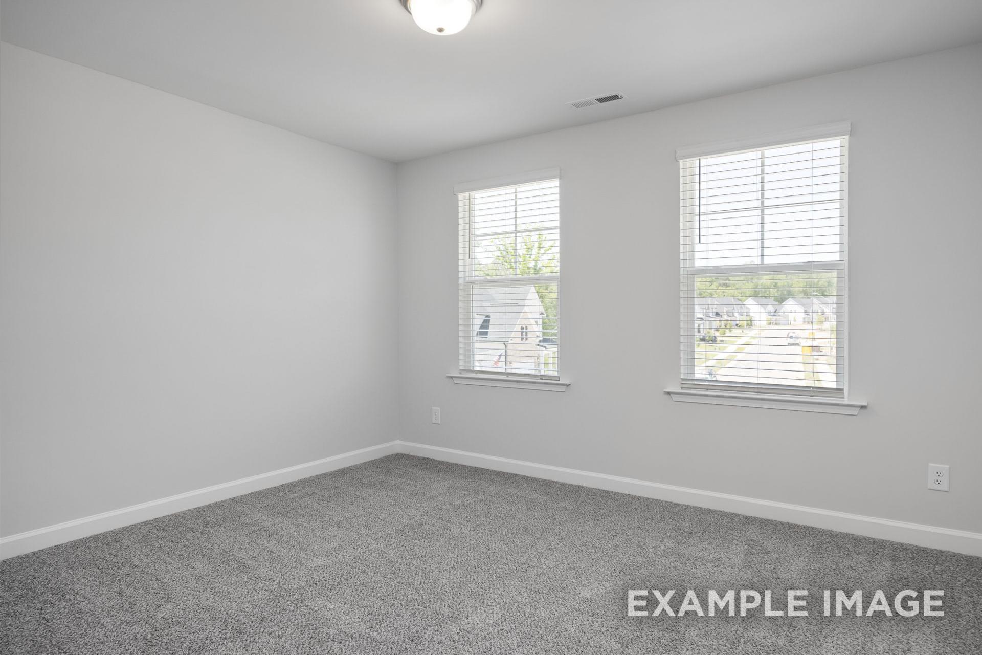Spacious upstairs bedroom in The Preston B with gray carpet, white walls, dual large windows with blinds overlooking neighborhood homes