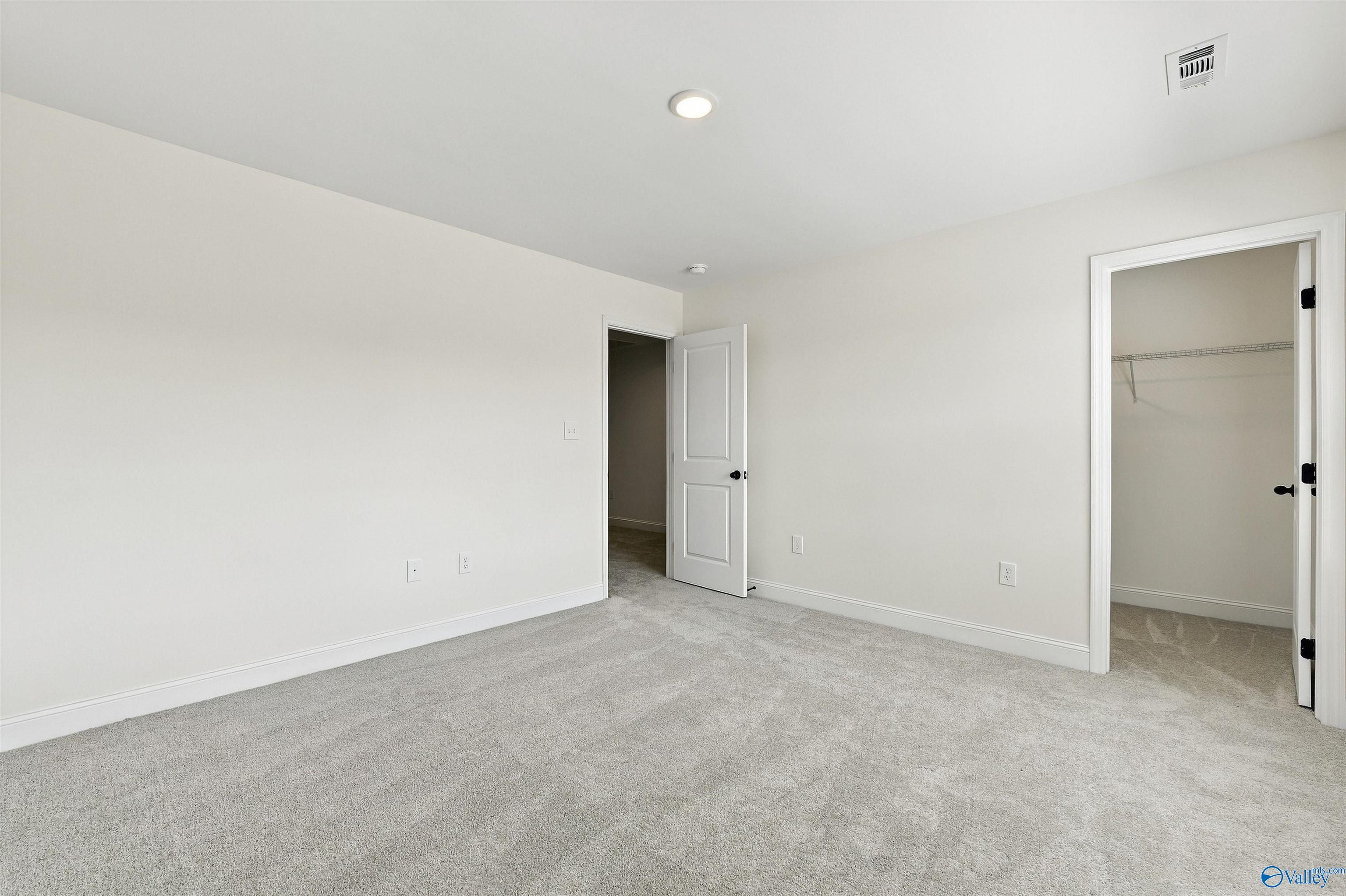 Spacious carpeted bedroom with white walls, walk-in closet, and recessed lighting in Davidson Homes' The Valencia, Huntsville, Alabama
