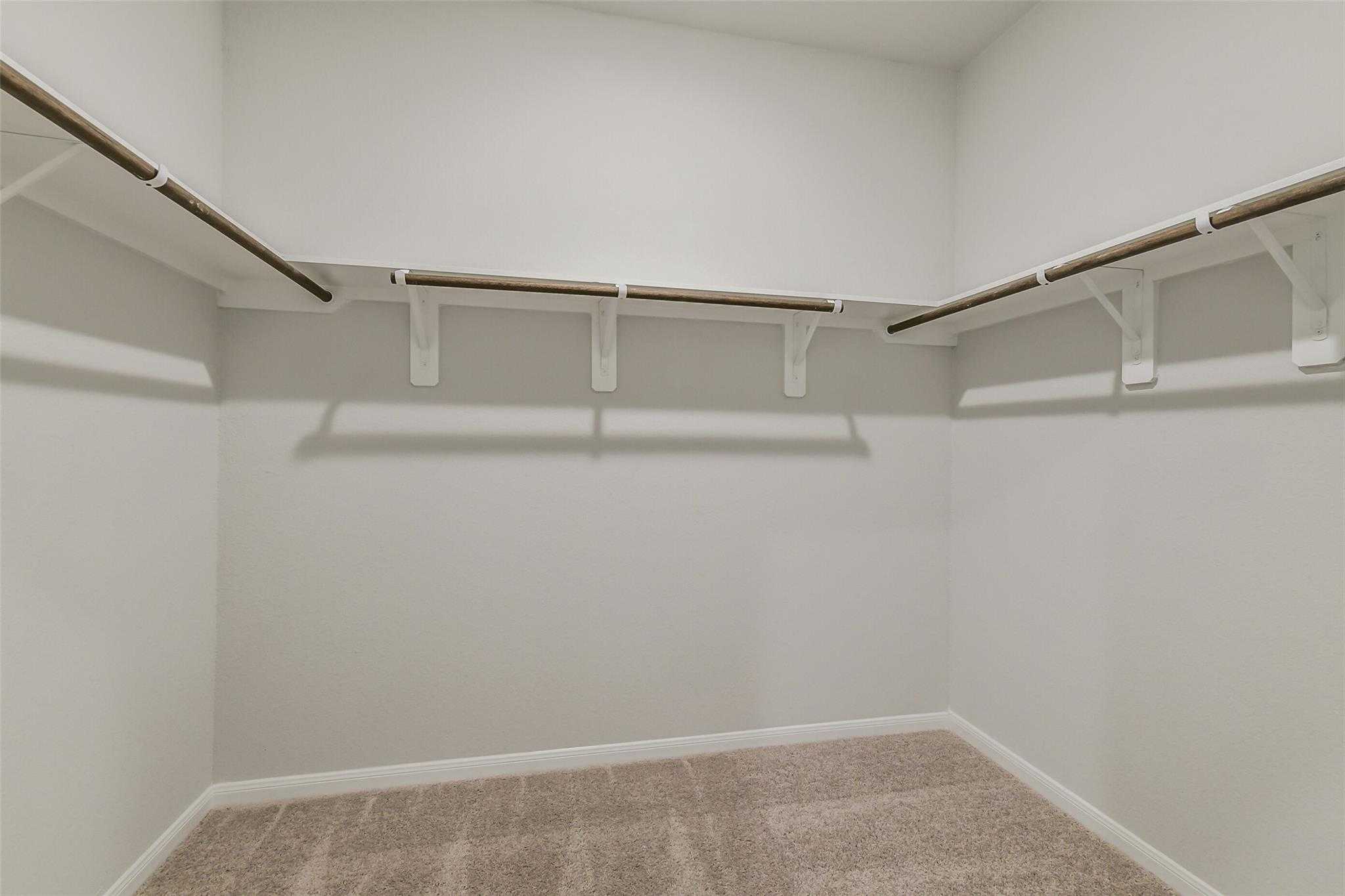 Spacious walk-in closet with built-in wooden shelves and hanging rods in master suite of Davidson Homes The Brazos F, Conroe TX