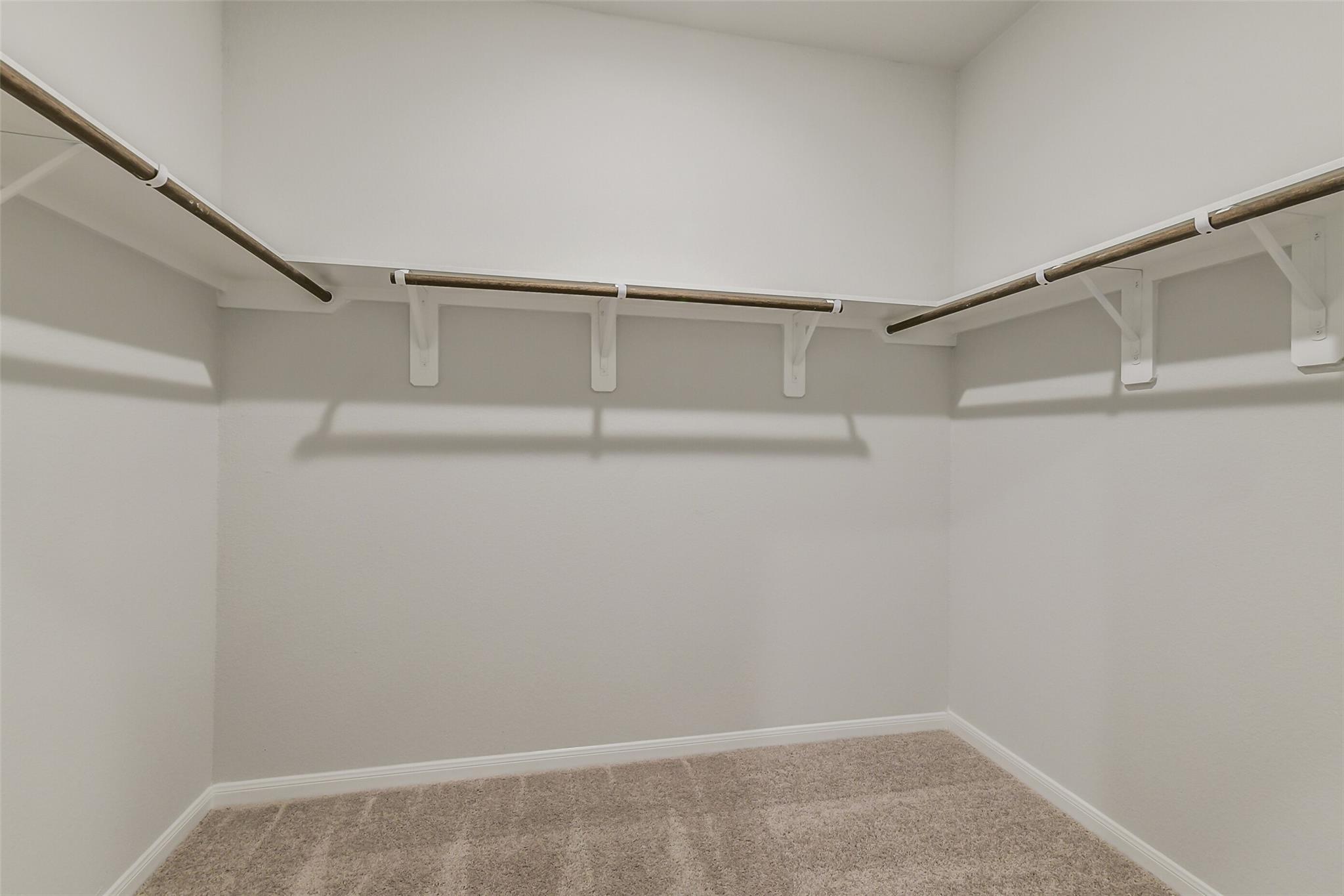 Spacious walk-in closet with wooden rods and shelving on white walls, beige carpet in Davidson Homes The Brazos F, Conroe, Texas